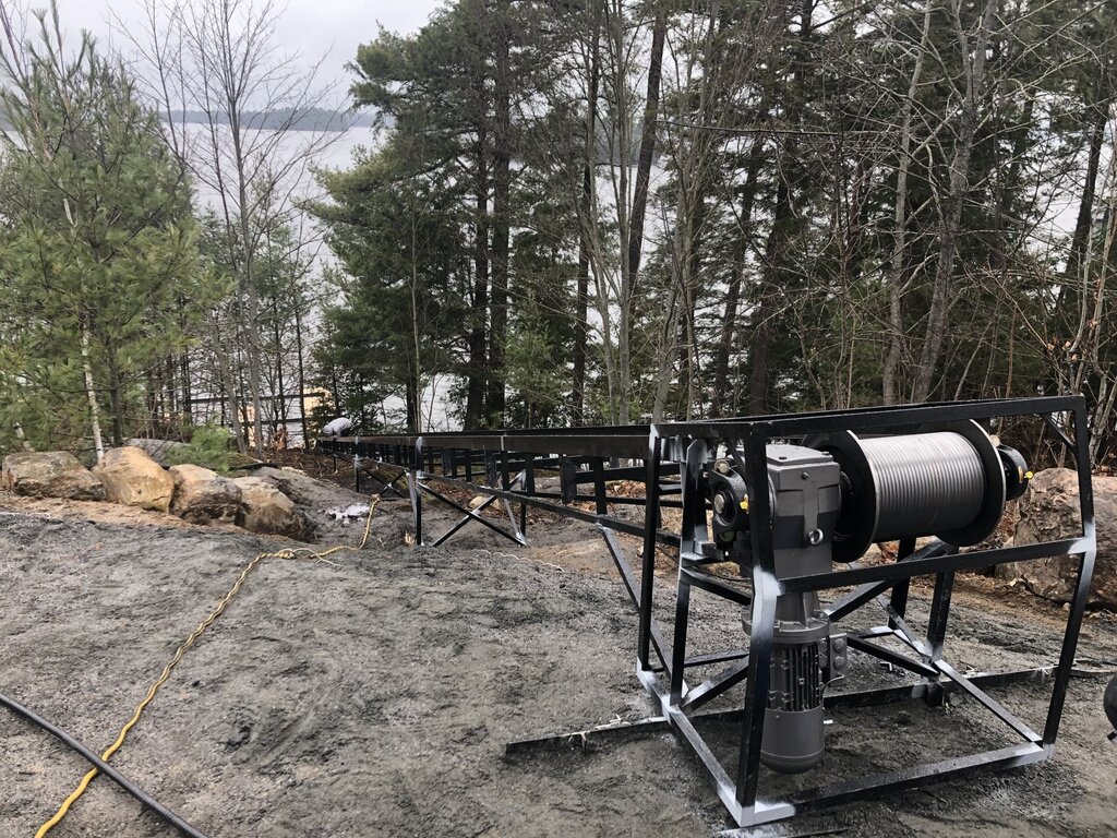 We kept the top end as close to the ground as possible to bring the upper station near the cottage. The station height was set by the height of the garage floor. Because the upper pitch is so shallow, there was no room for the control panel under the winch drum, so it is mounted inside the garage. Two Teck cables connect the panel to the lift—one carrying 240 V to the brake-motor, and a second carrying all the 24 V signal wires that control the car.